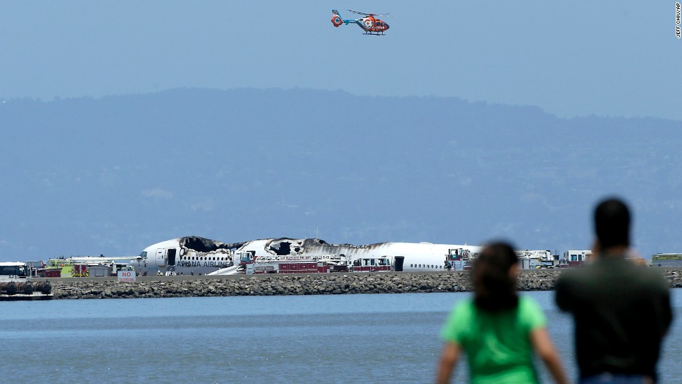 A helicopter flies above the wreckage on July 6 as people observe from across the waters of San Francisco Bay.