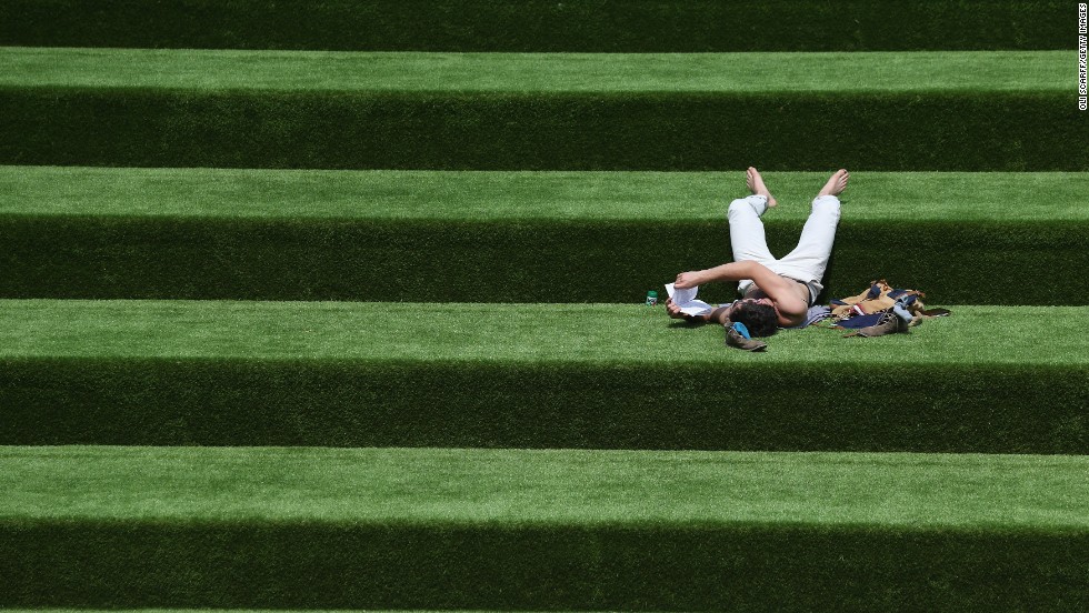 A man reads a book in the sunshine on steps covered in artificial grass on July 10 in London. 