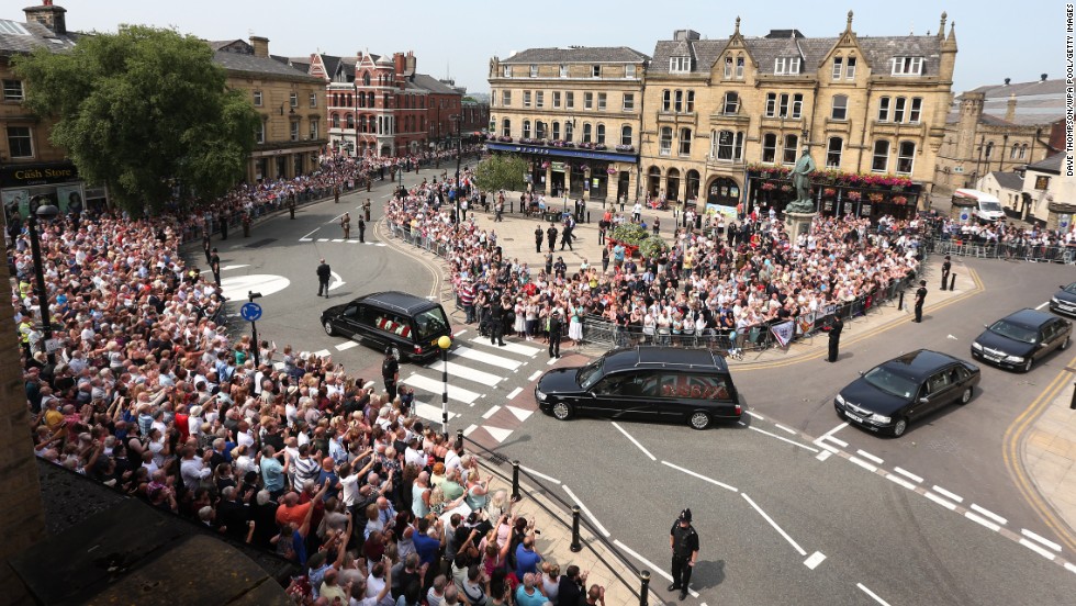 People line the streets to watch the funeral procession as it drives away from the church on July 12, in Bury, England.