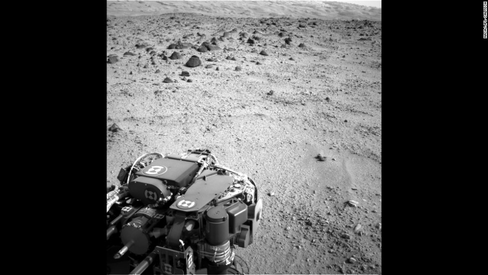 The lower slopes of &quot;Mount Sharp&quot; are visible at the top of this image, taken on July 9, 2013. The turret of tools at the end of the rover&#39;s arm, including the rock-sampling drill in the lower left corner, can also be seen. 