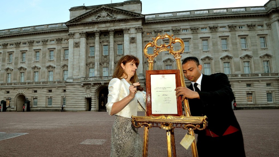 The queen&#39;s press secretary, Ailsa Anderson, left, and Badar Azim, a palace footman, place the official birth announcement on a golden easel in front of Buckingham Palace on July 22.