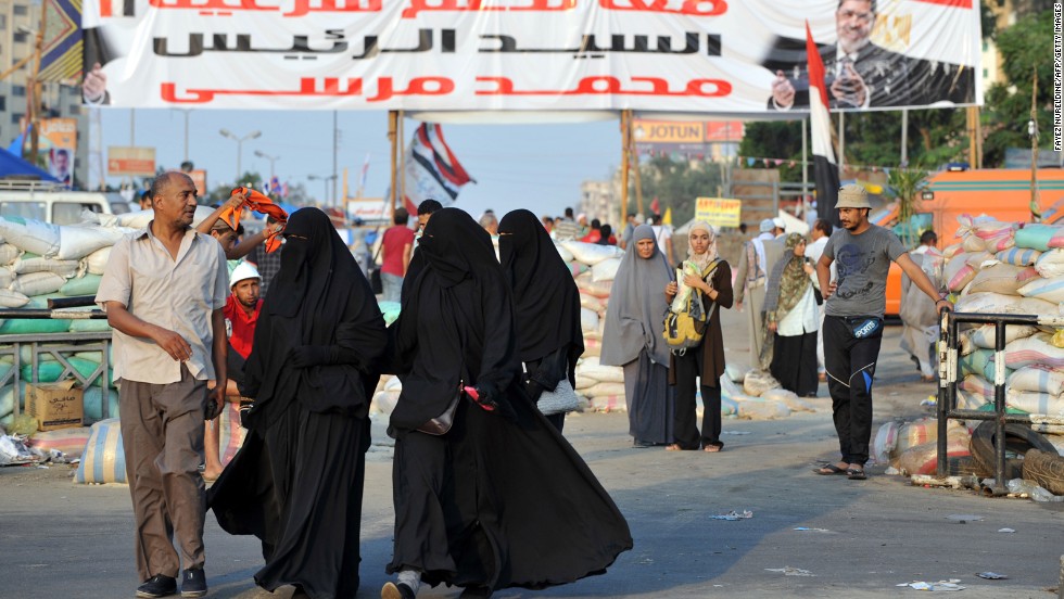 Morsy supporters walk past makeshift roadblocks at Rabaa al-Adawiya Square in Cairo on Saturday, August 3. Security forces set up the roadblocks outside the square, allowing people to leave but not enter, as they attempt to break up camps set up during ongoing protests over Morsy&#39;s ouster. 