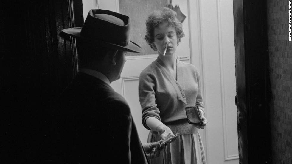 A woman buys ready-rolled marijuana cigarettes from a dealer at her door circa 1955.