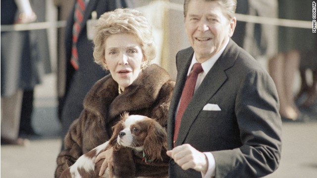 First Lady Nancy Reagan cradles an early Christmas present, a King Charles spaniel, as she and President Reagan stroll along the South Lawn of the White House in Washington on Friday, Dec. 6, 1985 after returning from New York. The new dog, a brother of a dog owned by National Review editor William Buckley Jr., is described as ?housebroken and extremely well-mannered.? (AP Photo/Dennis Cook)