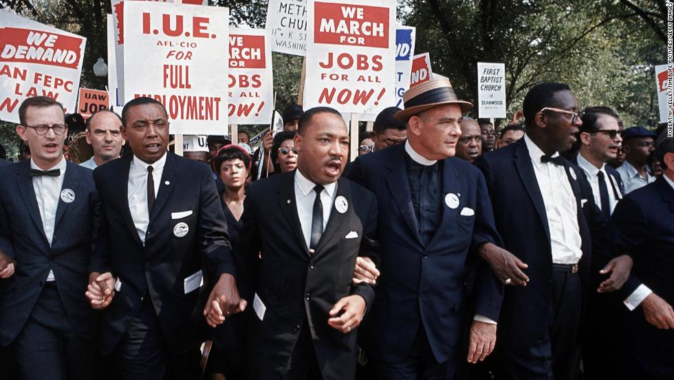 Leaders of the rally, including King in the center, interlock hands and arms as they march. The march was organized jointly by James Farmer, of the Congress of Racial Equality; Dr. King, of the Southern Christian Leadership Conference; John Lewis, of the Student Nonviolent Coordinating Committee; A. Philip Randolph, of the Brotherhood of Sleeping Car Porters; Roy Wilkins, of the National Association for the Advancement of Colored People; and Whitney Young, Jr., of the National Urban League.
