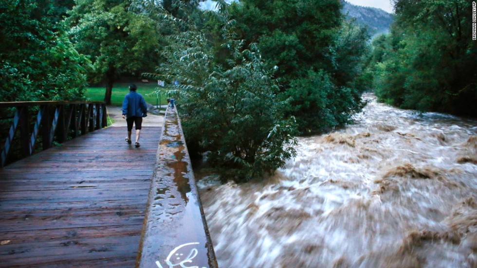 During a break in the rain, a woman walks over a footbridge past the raging Boulder Creek in Boulder on September 13. Boulder County is one of the hardest-hit areas.