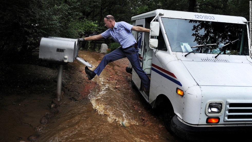 Dave Jackson closes a mailbox with his foot after delivering the mail to a home surrounded by water from the flooded Cheyenne Creek in Colorado Springs, Colorado, on Friday, September 13.