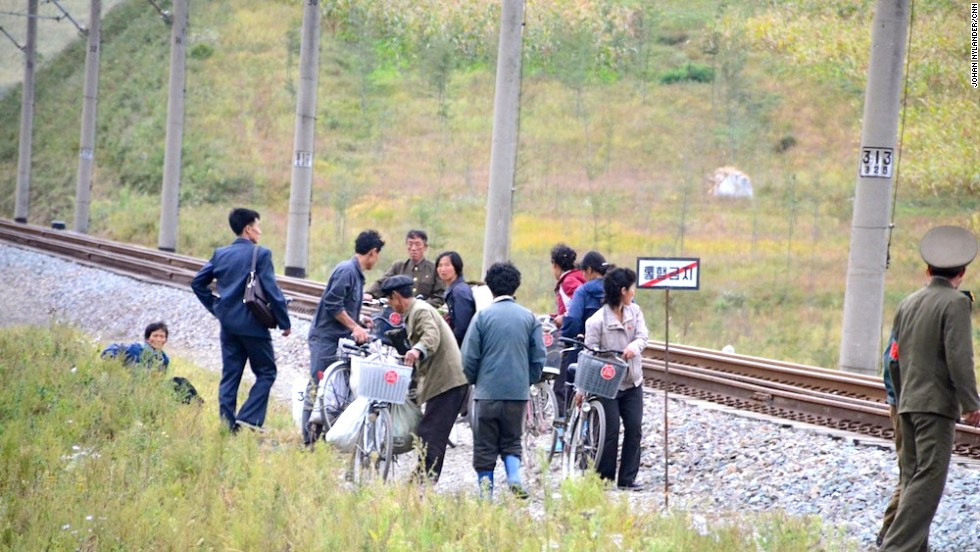 People standing by the train track, while a guard is monitoring the bike race. 