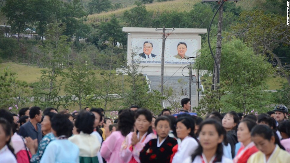 Spectators waiting for the bikers to reach the finish line. In the background the &quot;Great&quot; and &quot;Dear Leaders&quot; Kim Il Sung and his son, Kim Jong-Il.