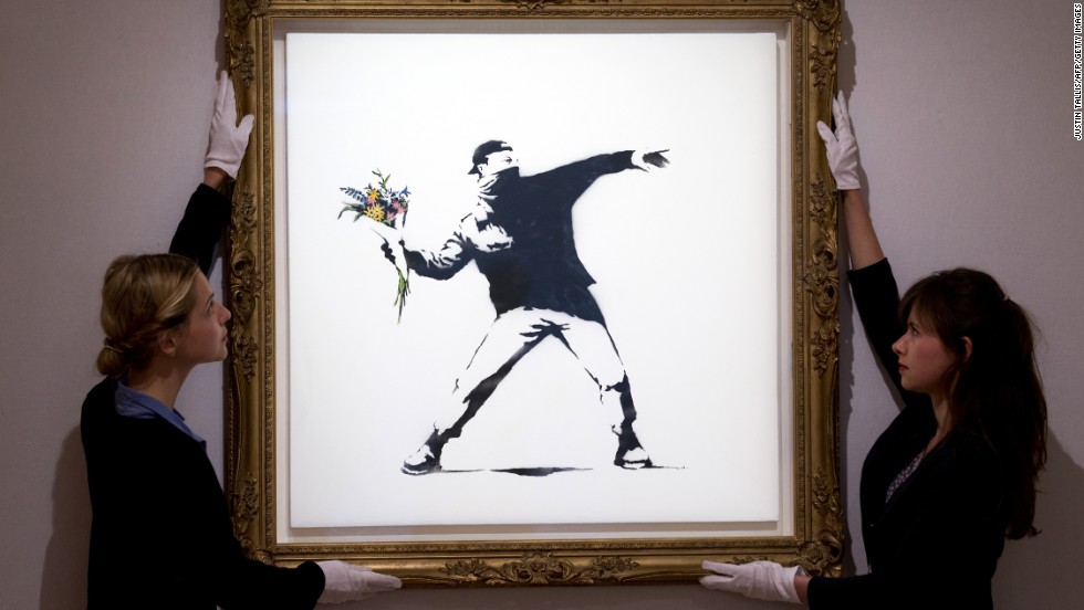 Gallery assistants adjust Banksy's &quot;Love Is in the Air&quot; ahead of an auction in London in June 2013. The piece was sold for $248,776.