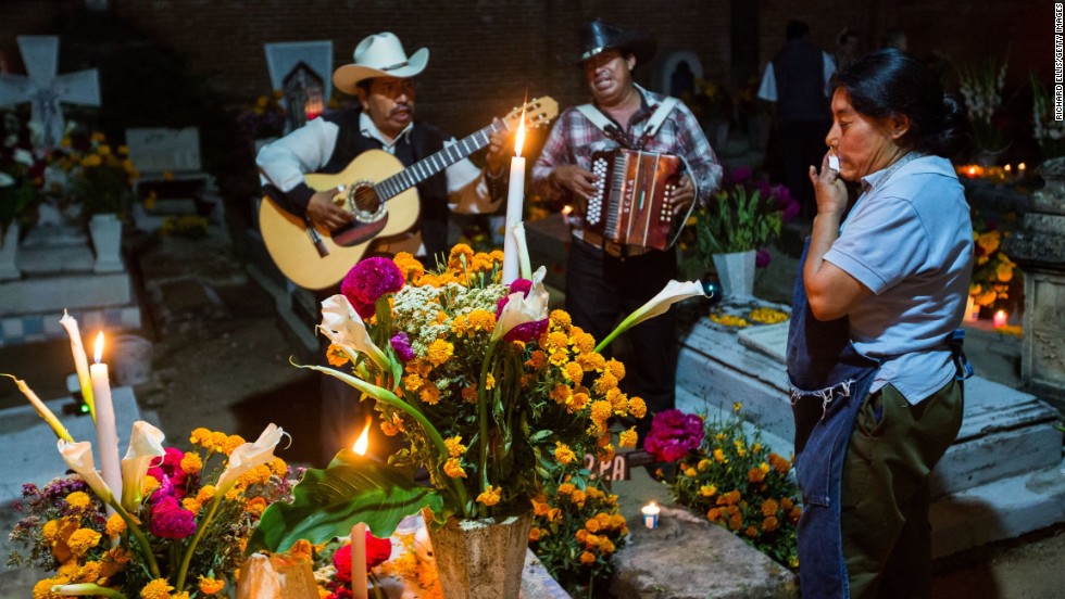 A Mexican woman wipes away a tear as a Mariachi band plays at the tomb of a loved one during the Dia de los Muertos, or Day of the Dead, festival in Oaxaca, Mexico, on Thursday, October 31. Celebrated in Mexico and around the world, the traditional holiday honors the lives of lost family members and friends.