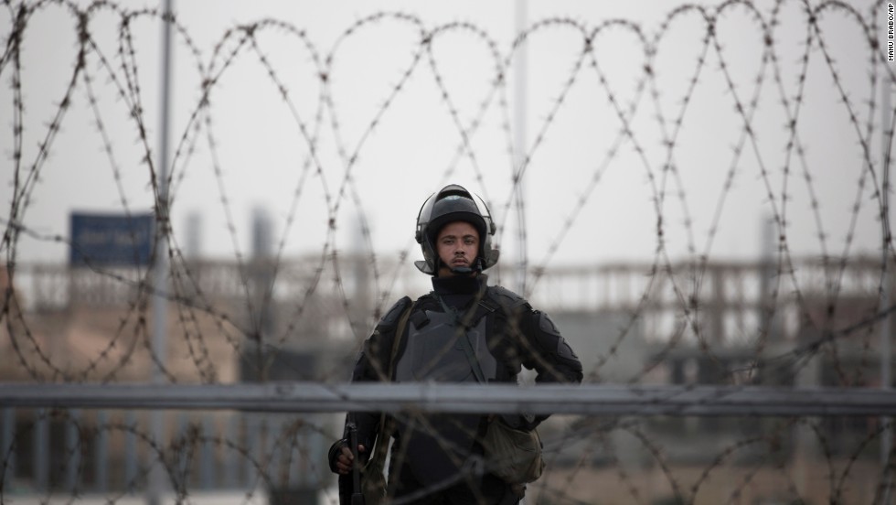 A police officer stands guard behind barbed wire.