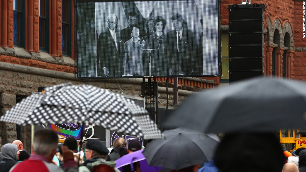 People near Dealey Plaza watch a historical broadcast about Kennedy&#39;s life.