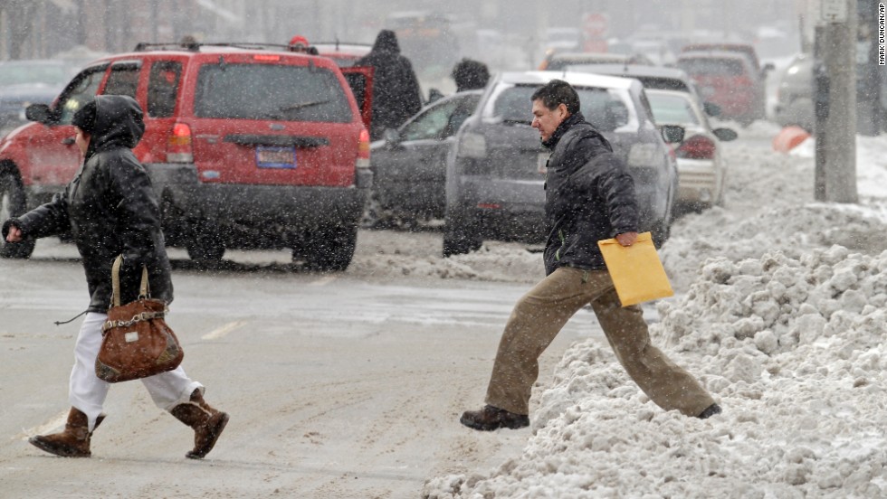 A man jumps off a snow-covered sidewalk to cross a downtown Cleveland street January 27. A minor car accident is in the background.