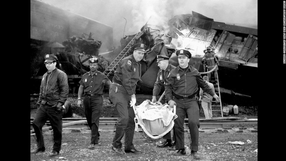 Patrolmen carry one of the dead from the wreckage caused when two trains crashed in a New York freight yard on May 22, 1967. Six crew members died and four more were injured.