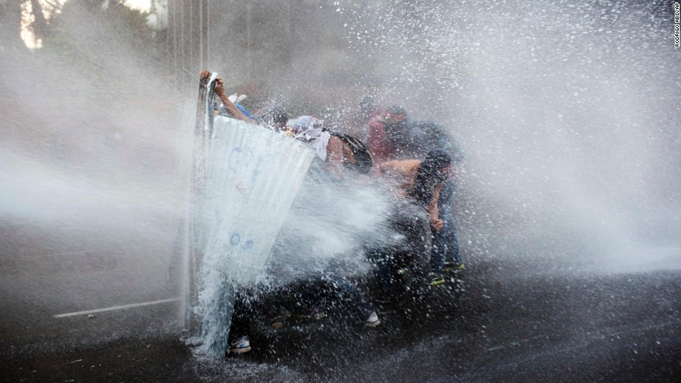 Protesters take cover from a police water cannon in Caracas on February 28.