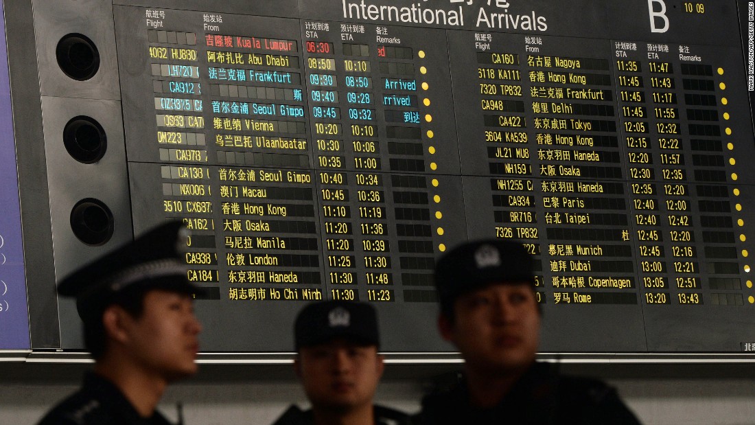 Chinese police at the Beijing airport stand beside the arrival board showing delayed Flight 370 in red on March 8, 2014.