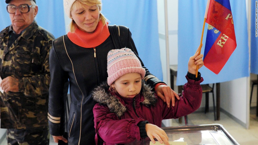 A child casts her mother&#39;s ballot March 16 while holding a Russian flag at a polling station in Simferopol.