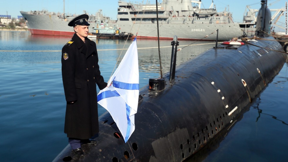 A Russian sailor holds the Russian Navy&#39;s St. Andrew&#39;s flag while standing on the bow of the surrendered Ukrainian submarine Zaporozhye on March 22 in Sevastopol.