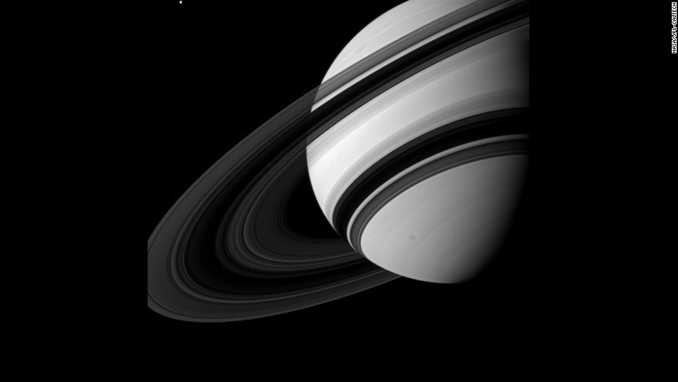 Tethys, top left, is dwarfed by Saturn as it orbits the planet, though scientists think the moon is much larger than Saturn&#39;s ring system.