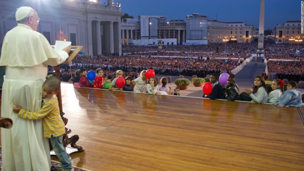 A young boy hugs Francis as he delivers a speech in St. Peter&#39;s Square in October 2013. The boy, part of a group of children sitting around the stage, played around the Pope as the Pope continued his speech and occasionally patted the boy&#39;s head.  