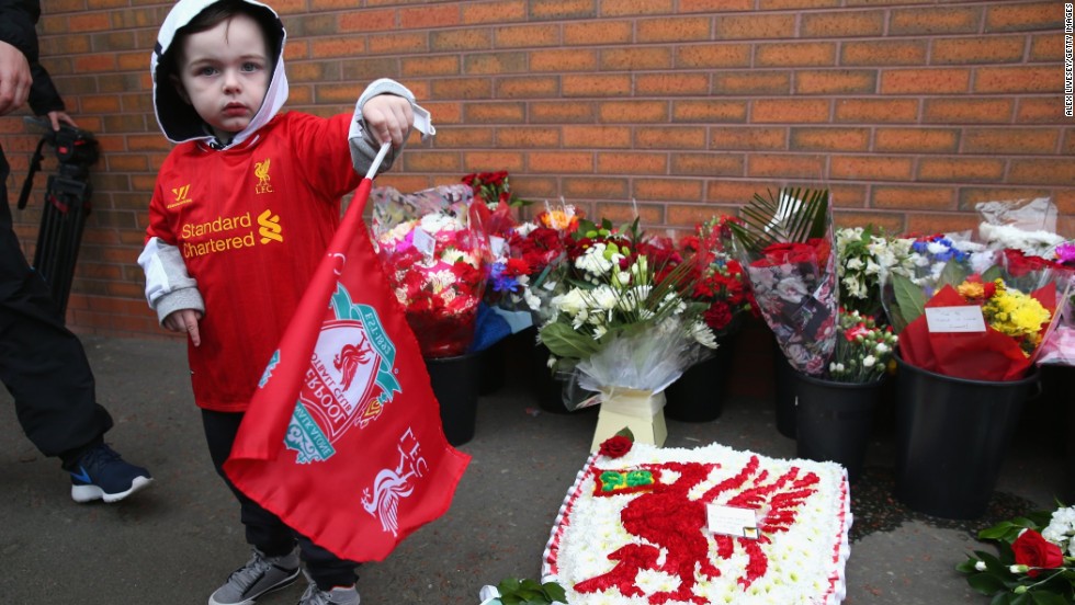 A young Liverpool fan stands next to floral tributes laid in memory of the victims on the 25th anniversary.