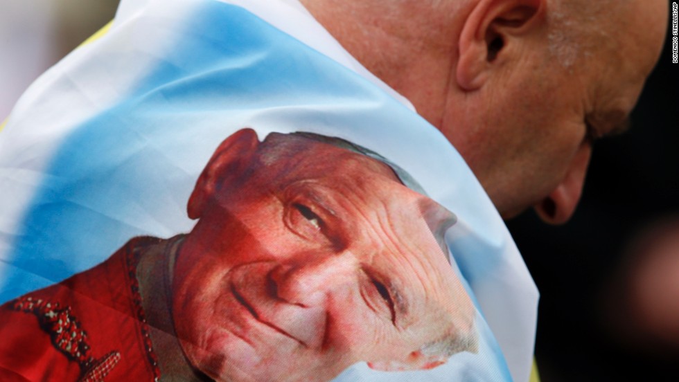 A man is wrapped in a flag bearing a picture of Pope John Paul II in St. Peter&#39;s Square.