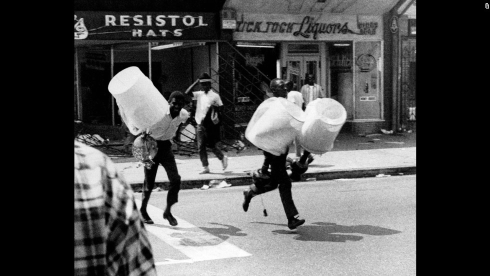 Two youths, carrying lampshades from a looted store, run down a street in the Watts neighborhood of Los Angeles on August 13, 1965. The Watts Riots were sparked by tensions between the city&#39;s black residents and police. The six days of violence left 34 dead and resulted in $40 million of property damage.