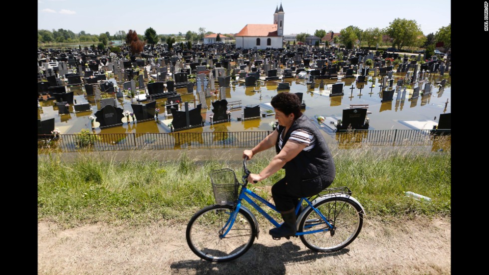 A woman rides a bicycle past a flooded cemetery in Domaljevac, Bosnia-Herzegovina, on Wednesday, May 21. 