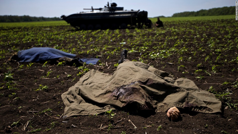 Bodies covered with blankets lie in a field near the village of Blahodatne, Ukraine, on May 22, as a Ukrainian soldier smokes next to his armored infantry vehicle.