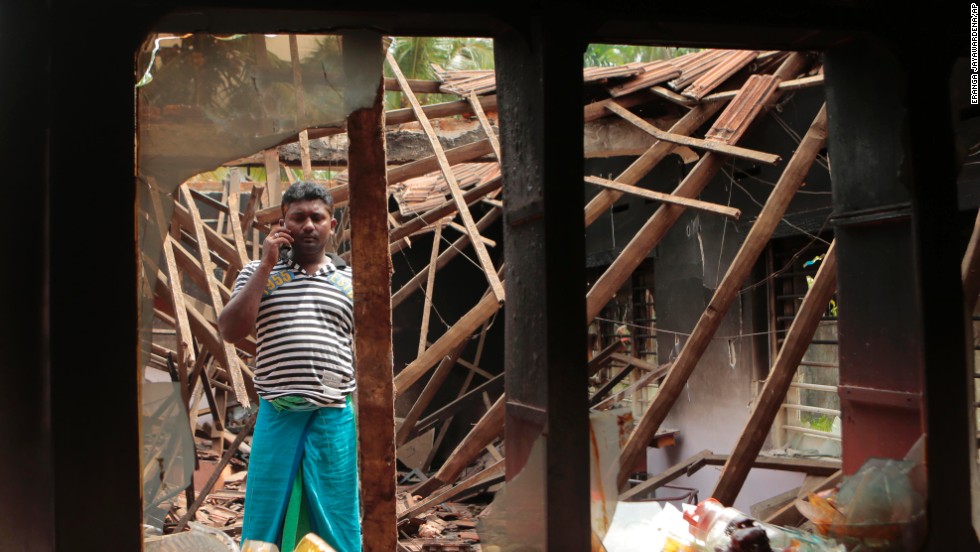 A Muslim man talks on his phone while standing in what&#39;s left of his house.