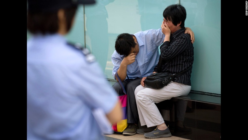 A police officer watches a couple cry outside the airline&#39;s office building in Beijing after officials refused to meet with them on June 11, 2014. The couple&#39;s son was on the plane.