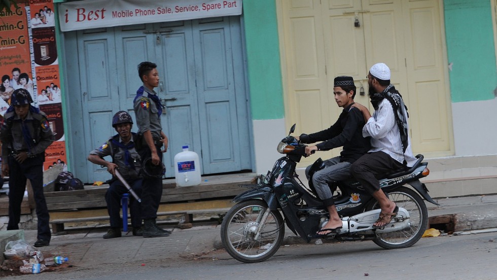Two Muslims ride past officers imposing order in the streets of Mandalay, Myanmar&#39;s multicultural, multi-faith second city. Muslims, who comprise about 5% of Myanmar&#39;s population, have been the target of occasional mob violence at the hands of the country&#39;s Buddhist majority in recent years,