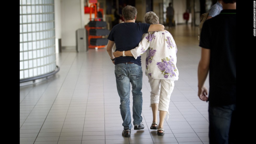 A couple walks to the location at Schiphol Airport where more information would be given regarding the flight.