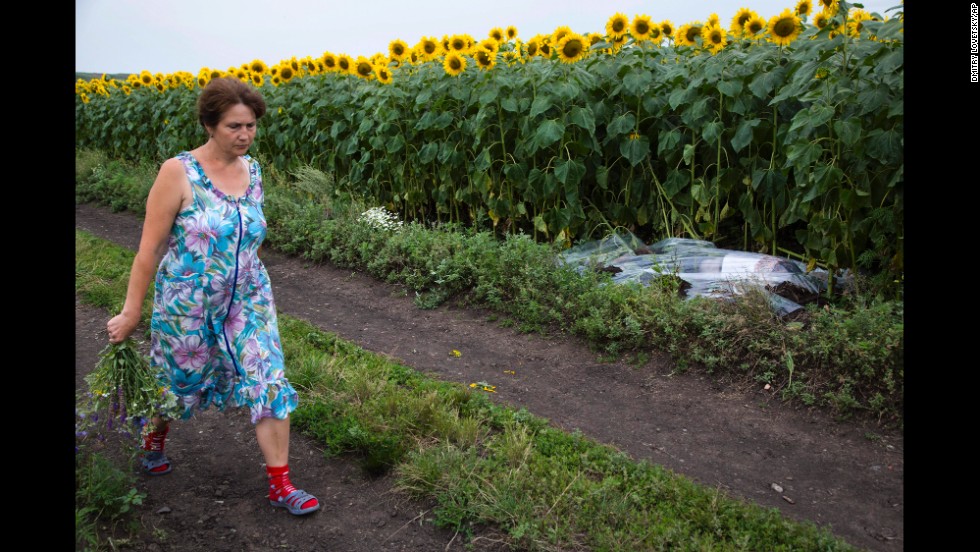 A woman walks past a body covered with a plastic sheet near the crash site July 18, 2014.