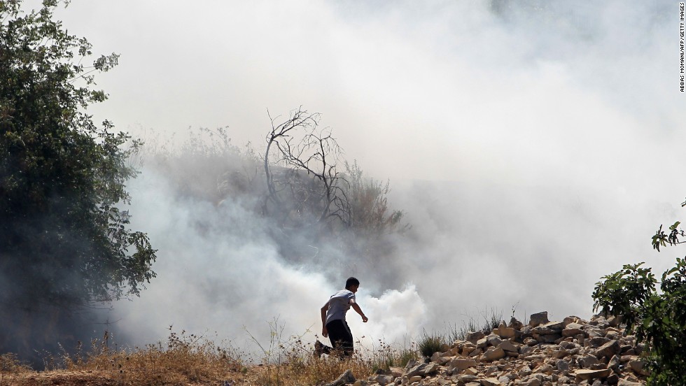 A Palestinian demonstrator, protesting Israel&#39;s military operation in Gaza, runs through smoke July 18 during clashes with Israeli soldiers at the entrance of the Ofer prison in the West Bank village of Betunia.