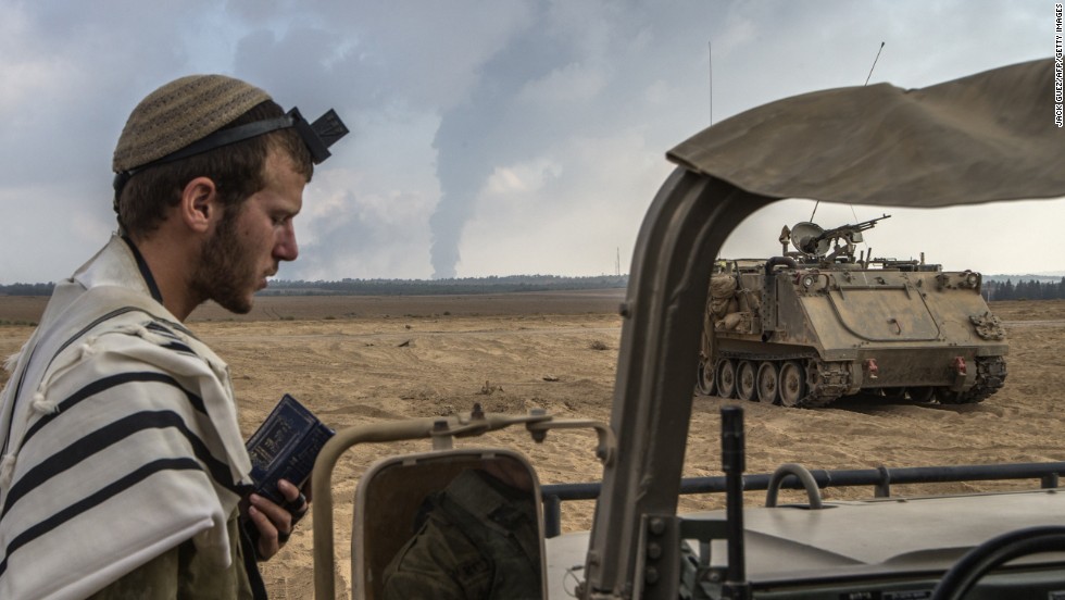 An Israeli soldier prays on the Israeli side of the border with Gaza on July 29 as smoke billows from the only power plant supplying electricity to Gaza.