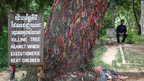 A Cambodian man sits in Choeung Ek Killing Fields near a tree that was used to beat children to death under the Khmer Rouge regime, on August 6, 2014 in Phnom Penh, Cambodia. 