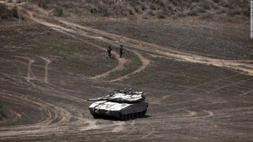 Israeli soldiers walk past a Merkava tank as they patrol a field near Israel&#39;s border with Gaza on August 9.