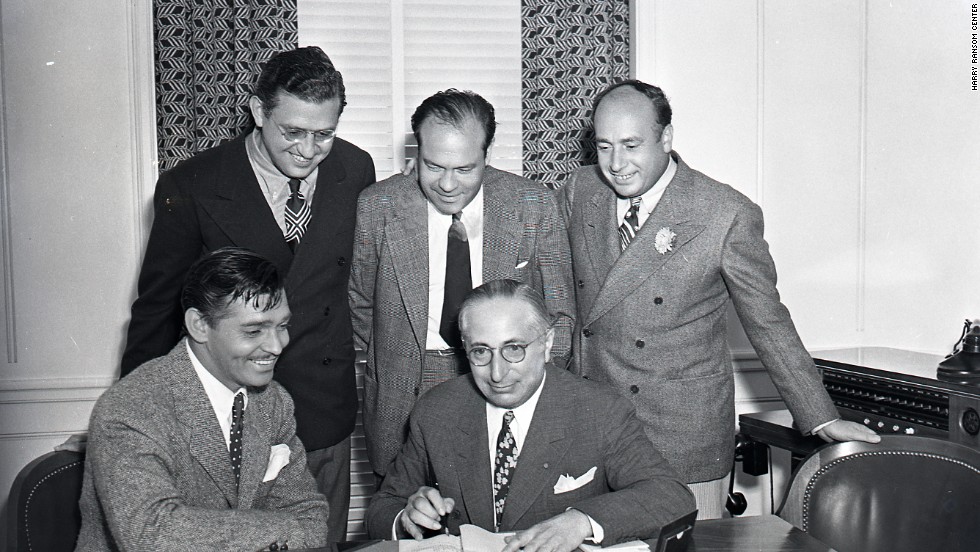 For publicity purposes, Clark Gable, the overwhelming popular choice to play Rhett Butler, pretends to sign a contract for the film under the watchful eye of producer Selznick, standing, far left, and MGM studio chief Louis B. Mayer, seated right. The star had been reluctant to tackle the role, fearing he wouldn&#39;t be able to live up to the public&#39;s expectations. With Gable now available, Selznick had to move quickly to start filming. 