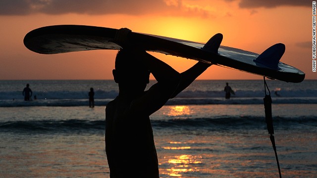 A Balinese surfer carries a surfboard at sunset along Kuta beach. 