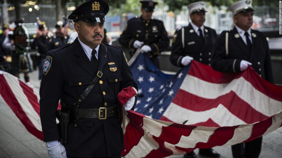 Members of the New York Police Department, the New York Fire Department and the Port Authority Police Department carry an American flag past one of the reflecting pools during memorial observances at the World Trade Center site.