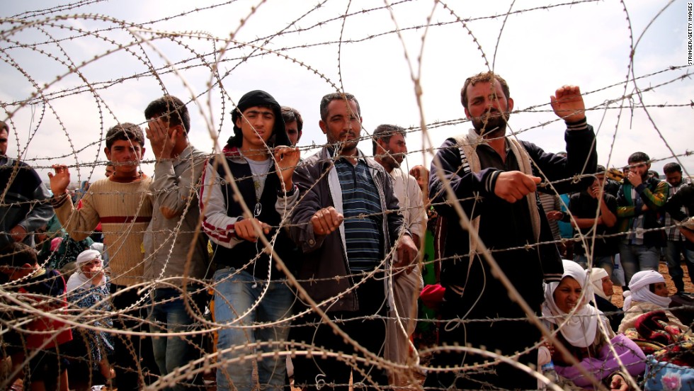Syrian Kurds wait behind border fences to cross into Suruc on Sunday, September 28.