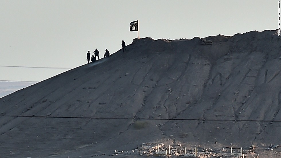 Alleged ISIS militants stand next to an ISIS flag atop a hill in Kobani on Monday, October 6. 