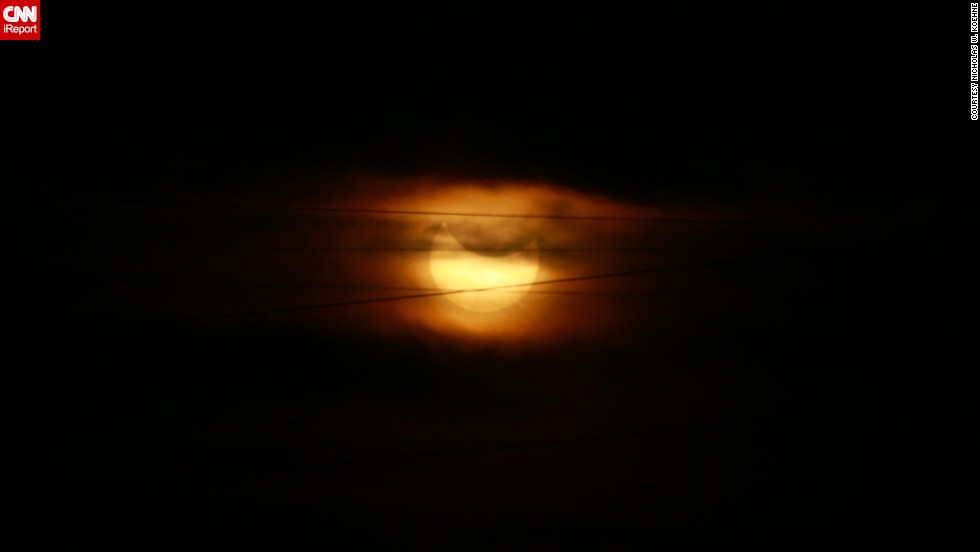 The partial eclipse &lt;a href=&quot;http://ireport.cnn.com/docs/DOC-1182662&quot;&gt;looms behind &lt;/a&gt;wispy clouds and a string of power lines in Topeka, Kansas.