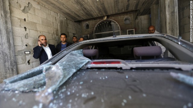 Fayez Abu Eitta, left,  a Fatah leader in Gaza, speaks on the phone as he inspects the damage to his car.