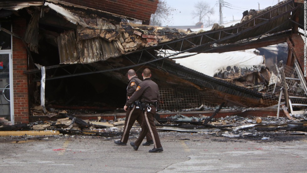 Police officers walk past the smoldering remains of a beauty supply store in Ferguson, Missouri, on Tuesday, November 25. Ferguson has been struggling to return to normal since Michael Brown, an unarmed black teenager, was killed by Darren Wilson, a white police officer, on August 9. The grand jury did not indict Wilson in the case, prompting new waves of protests in Ferguson and &lt;a href=&quot;http://www.cnn.com/2014/11/25/justice/gallery/national-ferguson-protests/index.html&quot;&gt;across the country.&lt;/a&gt;
