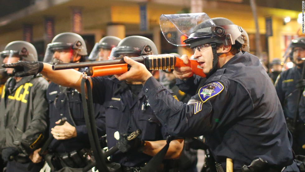 A police officer raises a shotgun toward the crowd in Berkeley on Saturday, December 6.