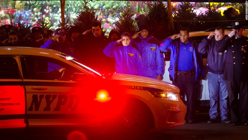 Mourners stand at attention as the bodies of two fallen NYPD officers are transported from Woodhull Medical Center on Saturday, December 20. 