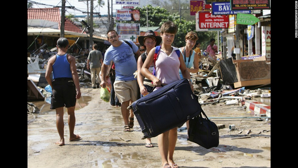 Travelers walk past devastation, carrying their luggage, as they head to the airport on December 27, 2004. Patong Beach was one of the worst hit provinces of Phuket, Thailand. 